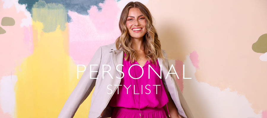 A smiling woman with blonde wavy hair stands against a pastel abstract painted background, wearing a bright pink outfit with a light gray blazer. Large white text across the center reads 'PERSONAL STYLIST'.